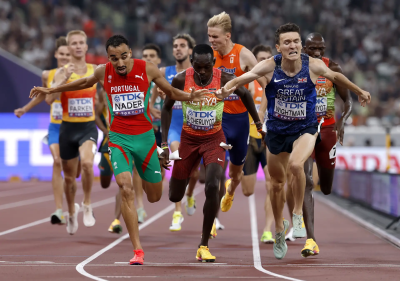 Atletas a correr numa pista de atletismo em competição com uniformes coloridos e textos visíveis