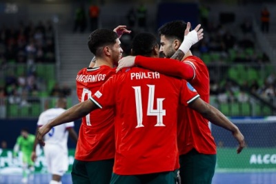 Jogadores de futebol com camisolas vermelhas com nomes e números brancos nas costas abraçados em campo