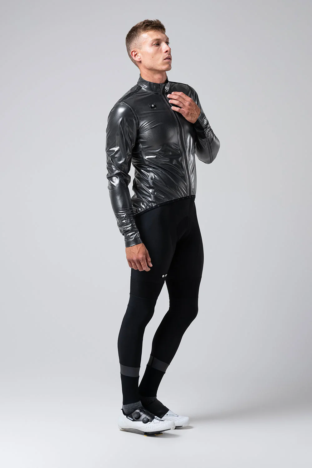 Homem vestido com roupa preta de ciclismo e sapatos brancos num fundo cinzento