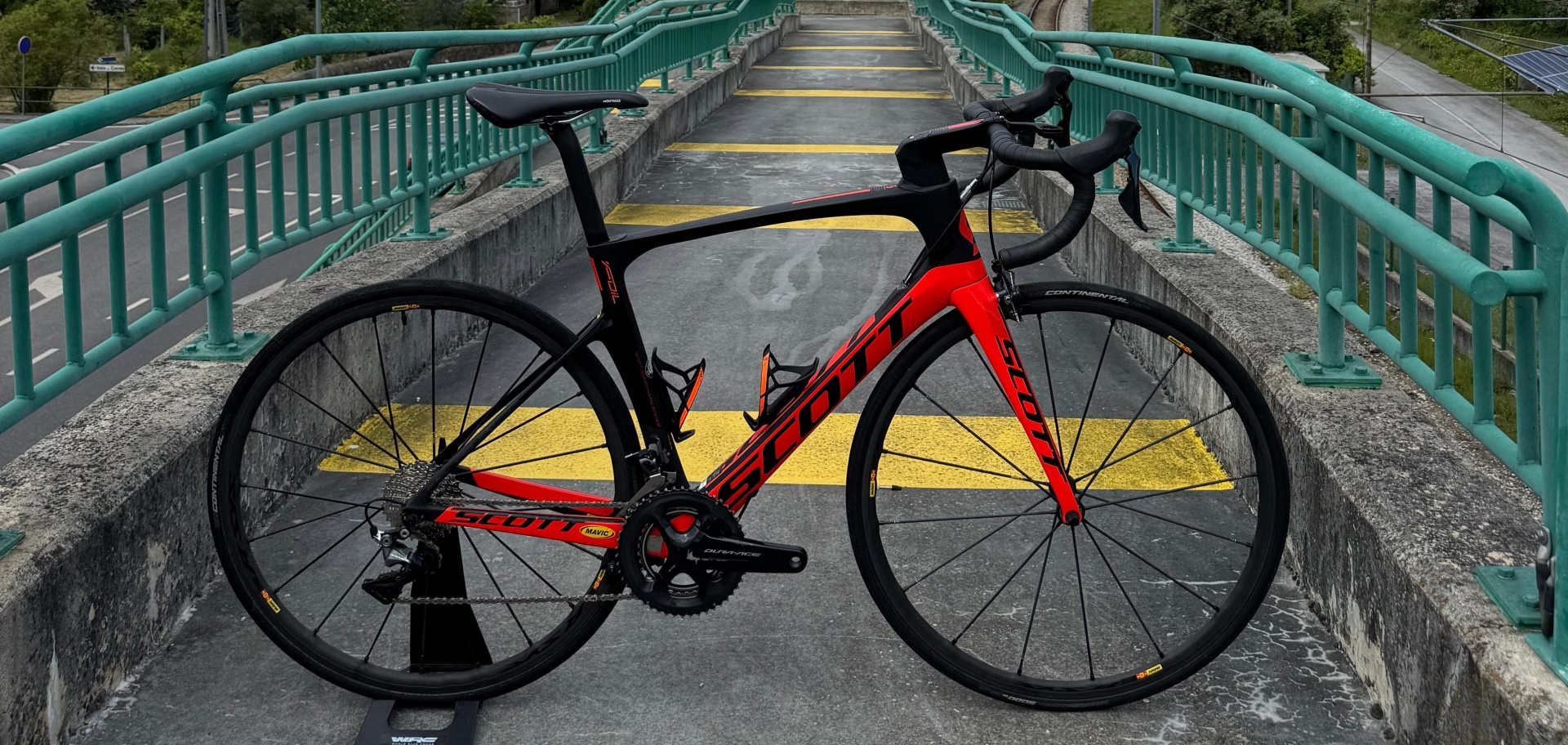 Bicicleta de estrada preta e vermelha numa passadeira com corrimãos verdes