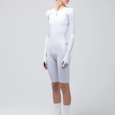 Pessoa em roupa desportiva branca justa, com luvas e meias, em fundo cinzento neutro.