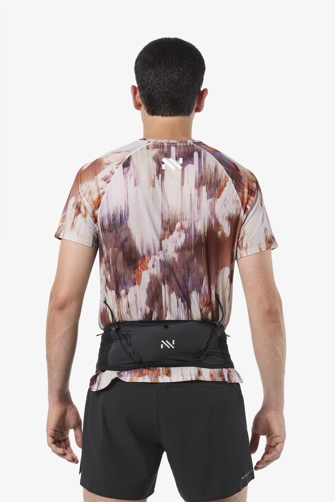 Homem visto de costas com t-shirt de padrão abstrato em castanho e calções pretos