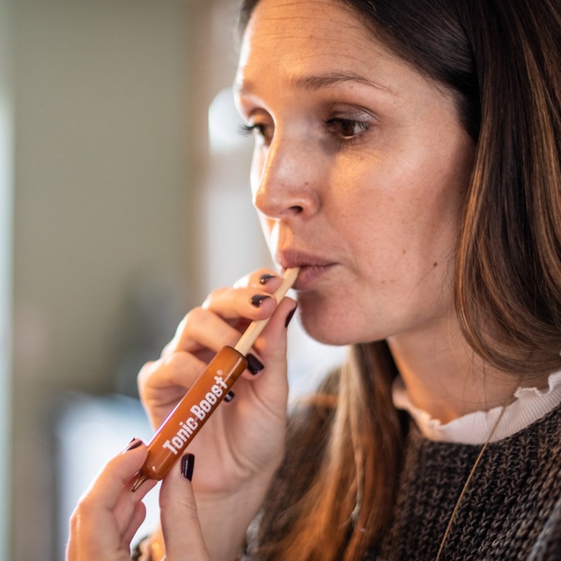 Mulher a usar dispositivo portátil Tonic Boost cor de ferrugem na boca