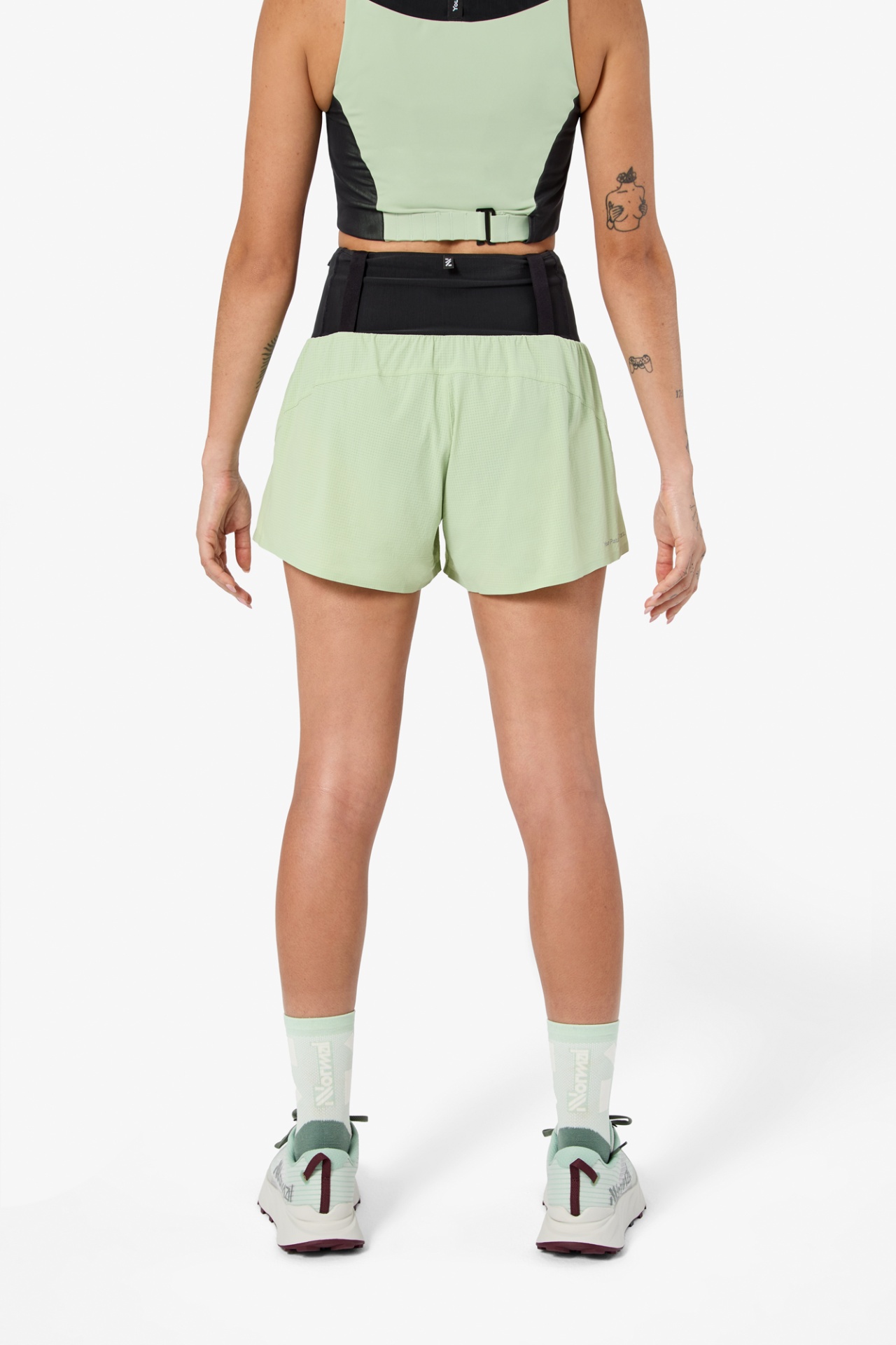 Mulher de costas com roupa desportiva verde claro e preta, meias e sapatilhas coordenadas.