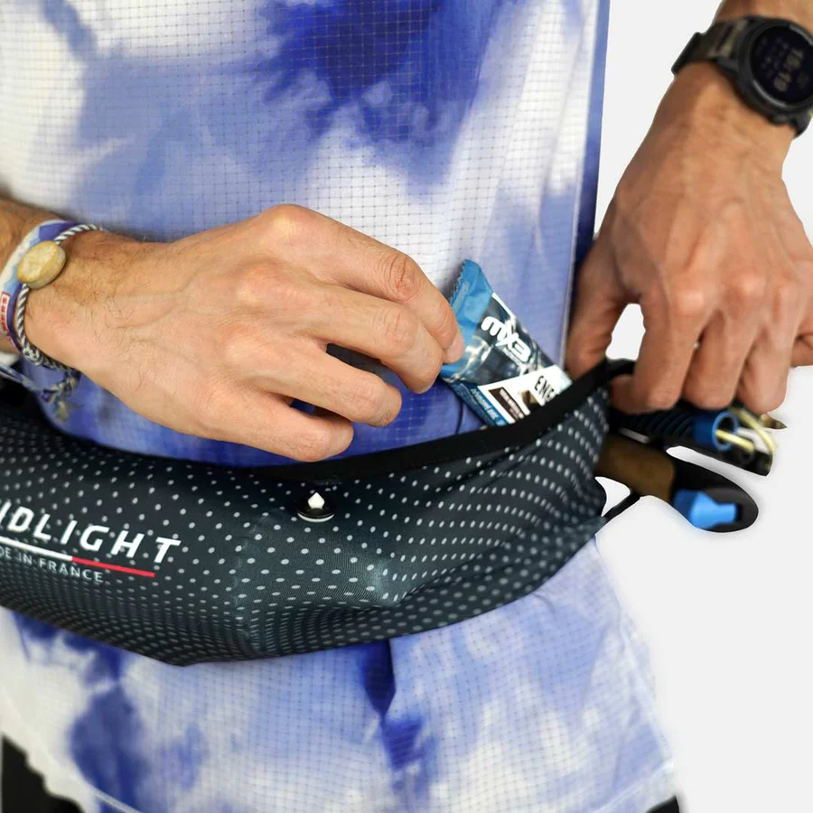 Saco de cintura preto com pontos brancos e barra energética azul numa mão