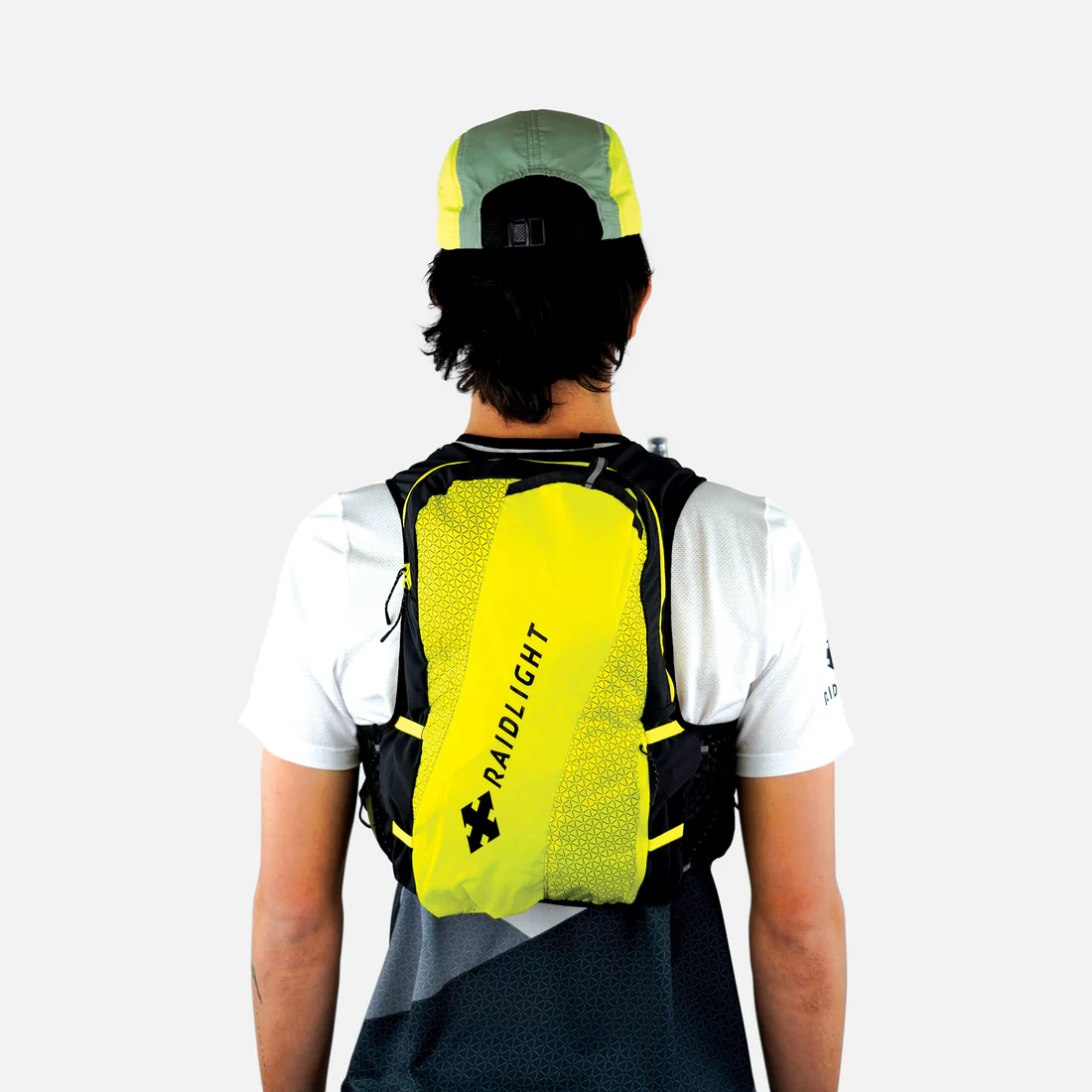 Mochila desportiva amarela e preta RAIDLIGHT vista de costas numa pessoa com t-shirt branca e boné verde e amarelo