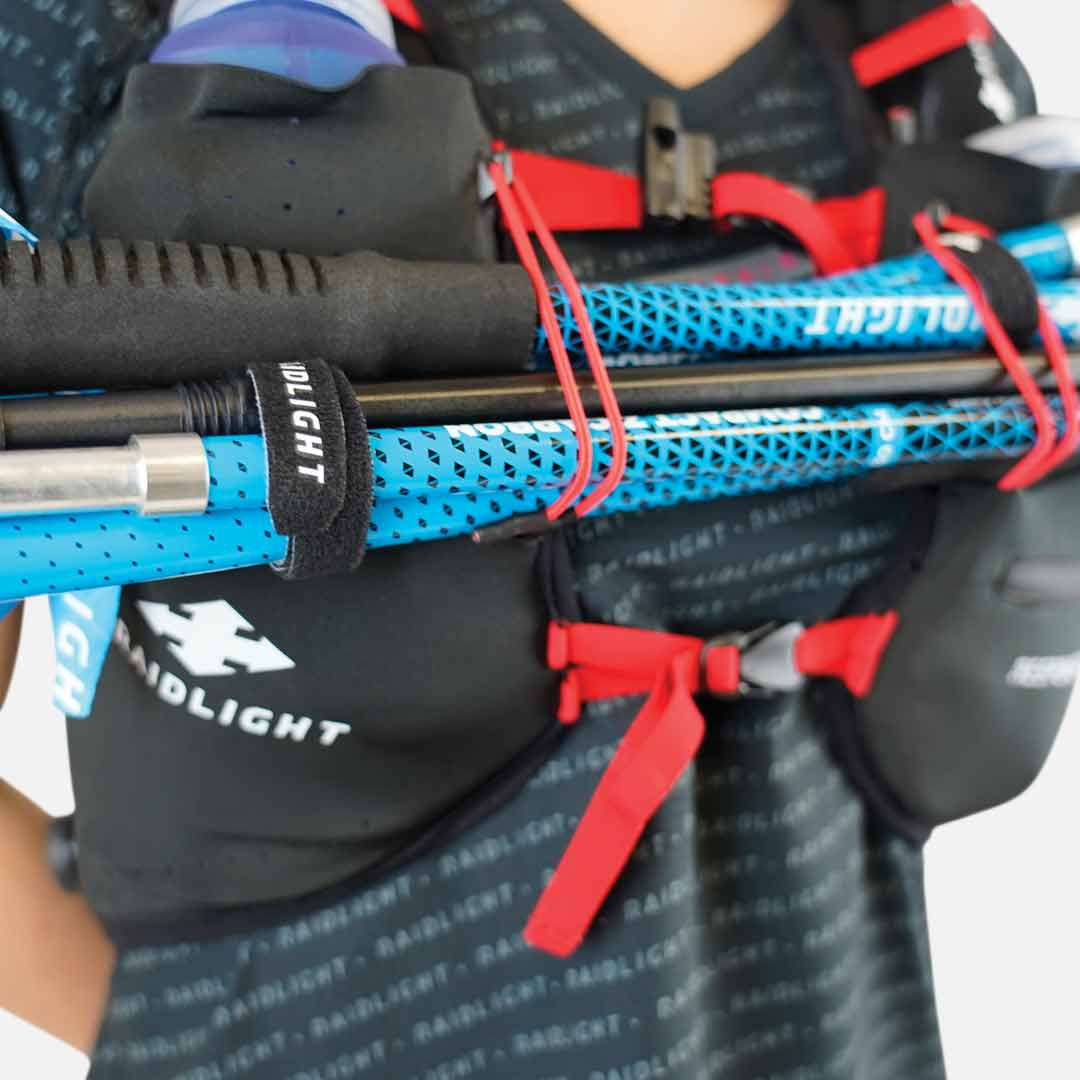 Colete de hidratação preto com bastões de trekking azuis e detalhes em vermelho