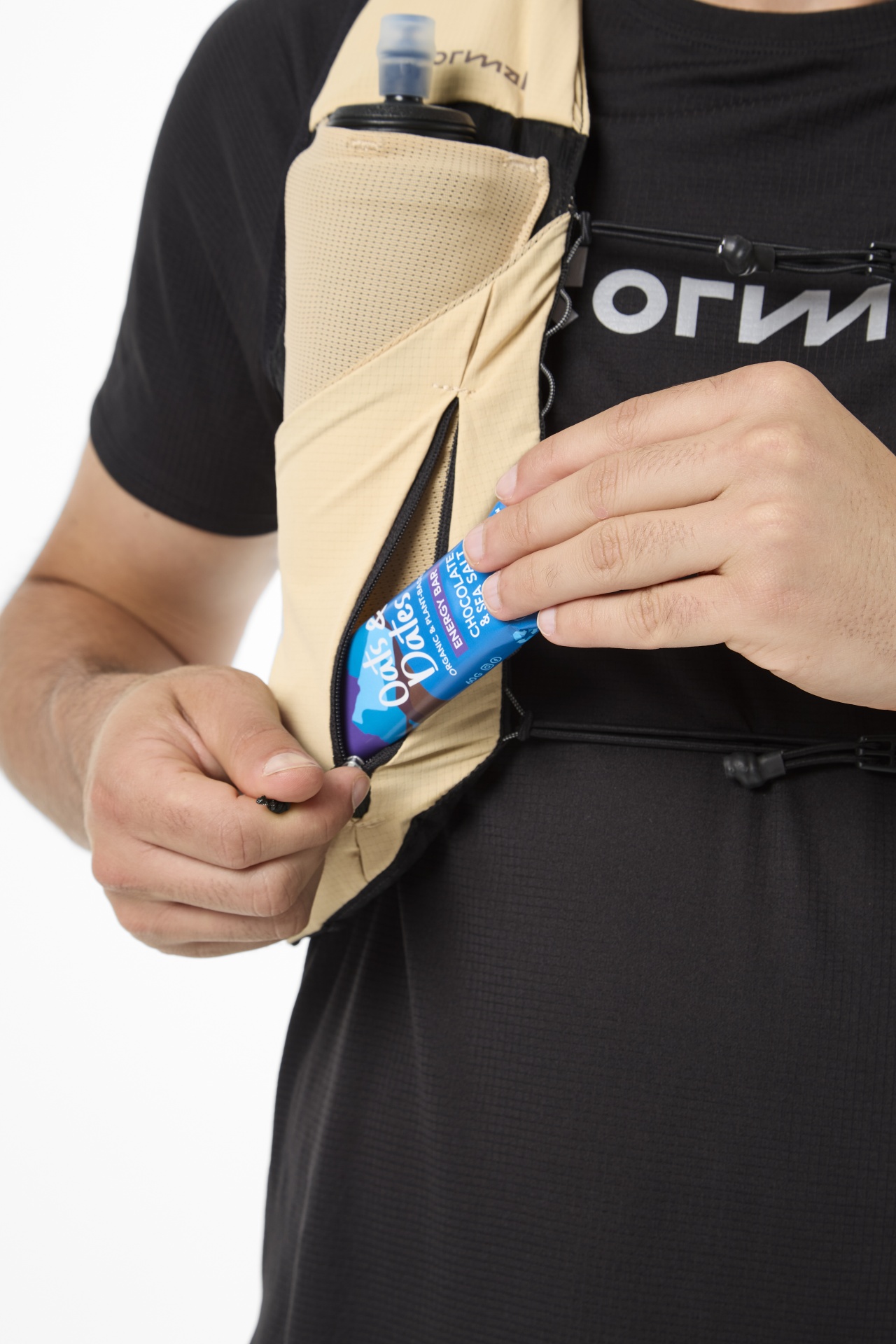 Homem com colete desportivo bege guardando barra energética azul no bolso com fecho, veste t-shirt preta.
