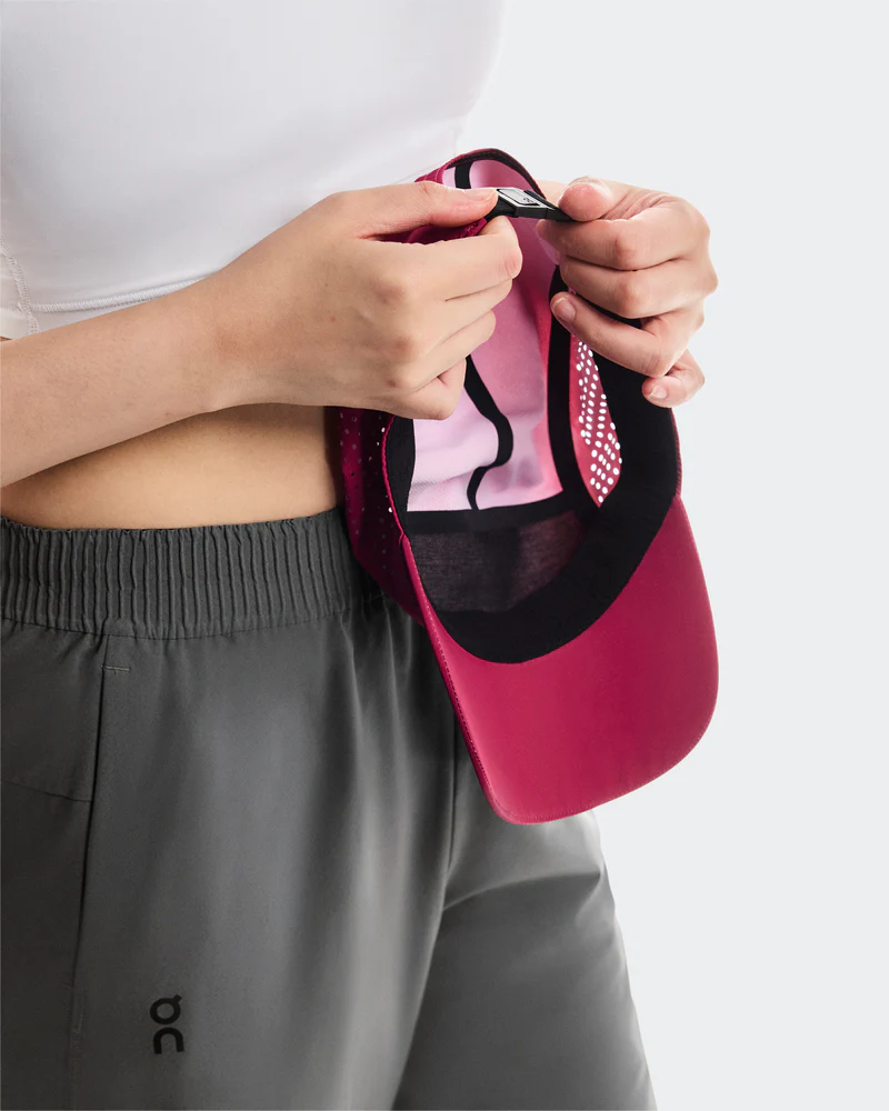 Pessoa a vestir calças cinza e a segurar viseira vermelha desportiva