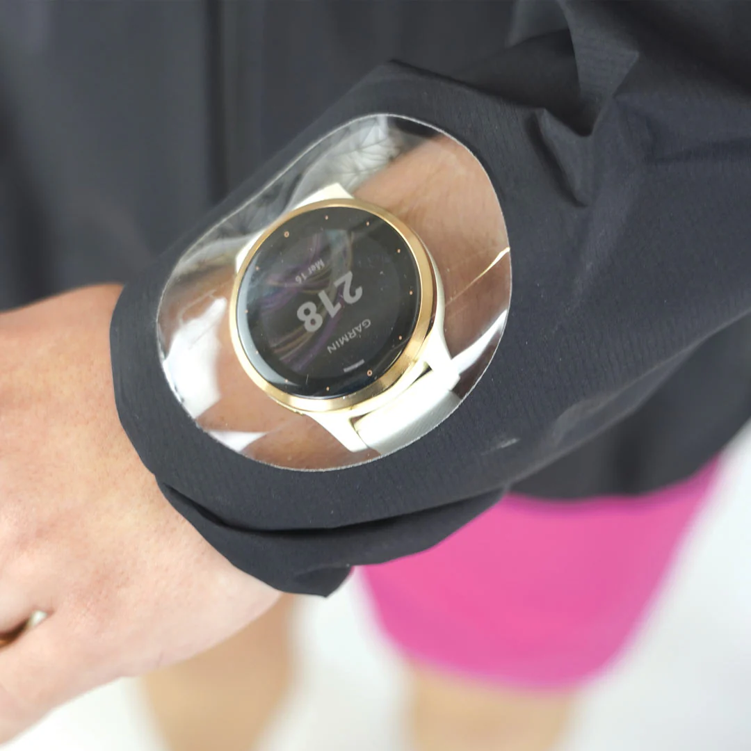 Relógio Garmin dourado com bracelete branca num pulso com manga preta