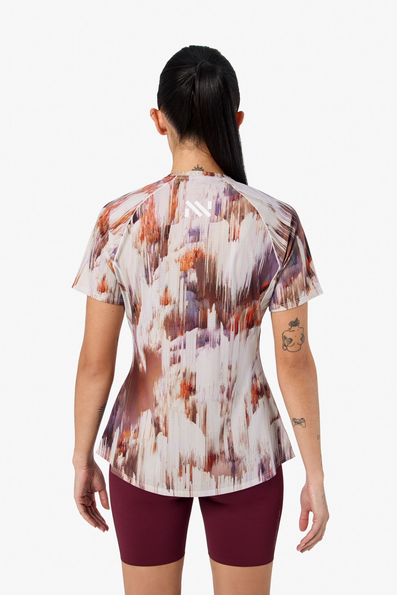 Mulher de costas com t-shirt colorida e calções bordô em fundo branco