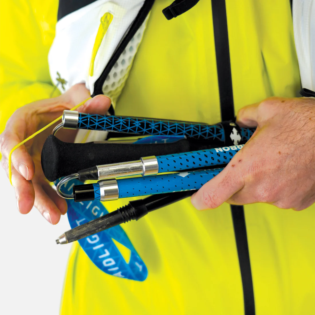 Pessoa segura bastões dobráveis azuis e pretos com cordão azul, vestindo casaco amarelo.