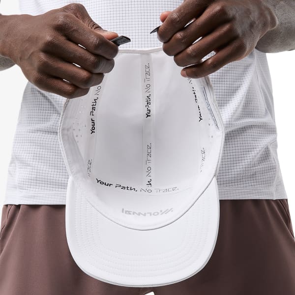 Boné branco com texto interno e logótipo na aba segurado por pessoa com roupa desportiva