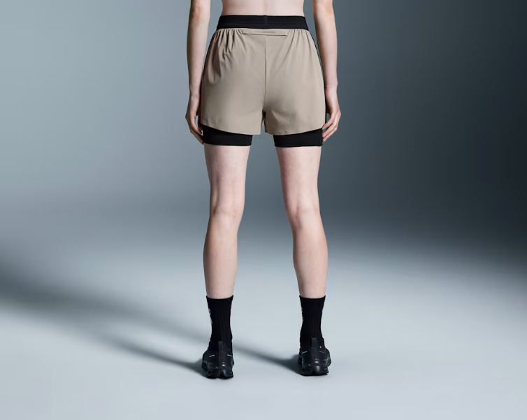 Pessoa de costas com calções de desporto bege e preto, meias e sapatilhas pretas