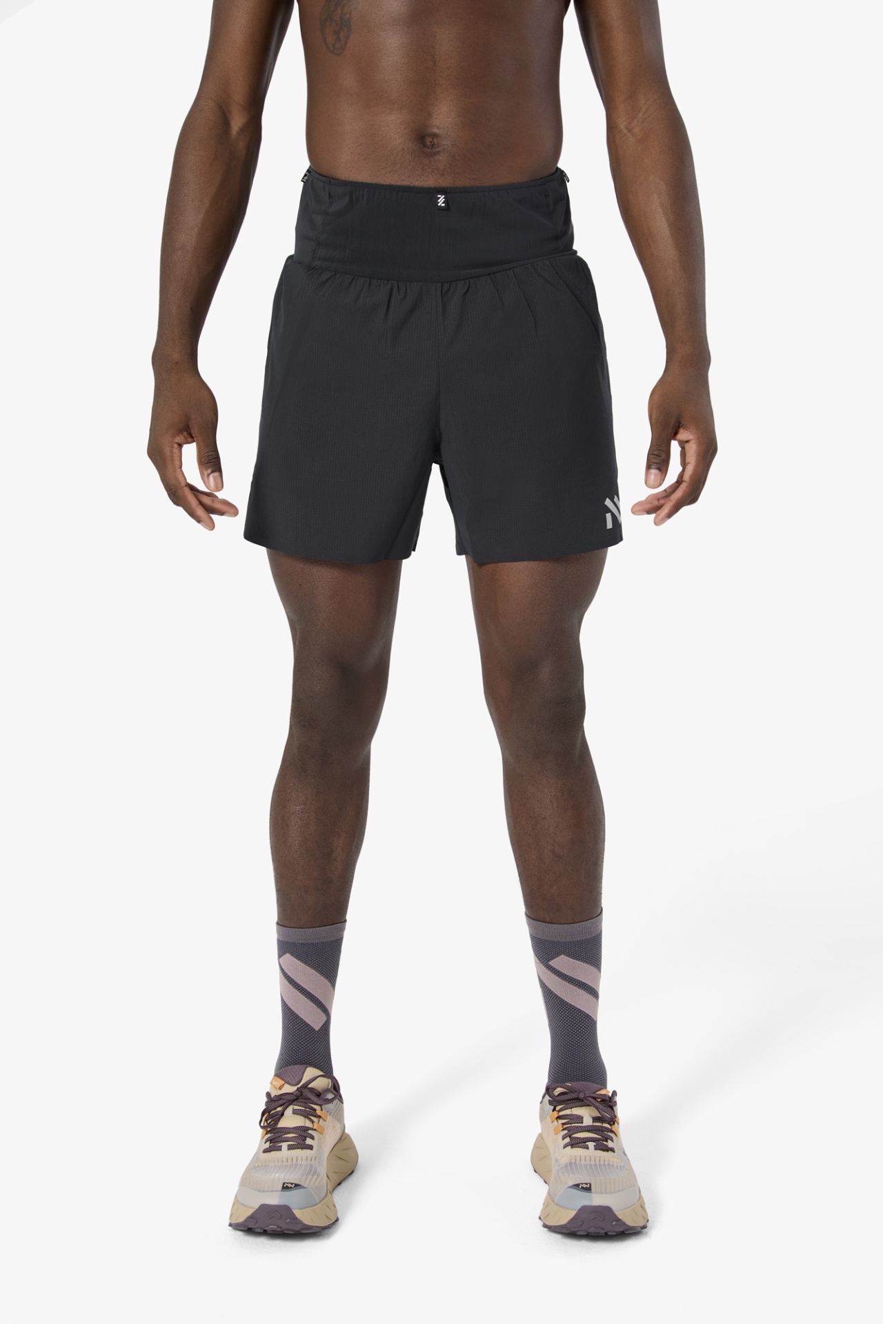 Pessoa com calções pretos, meias cinzentas e sapatilhas bege em fundo branco