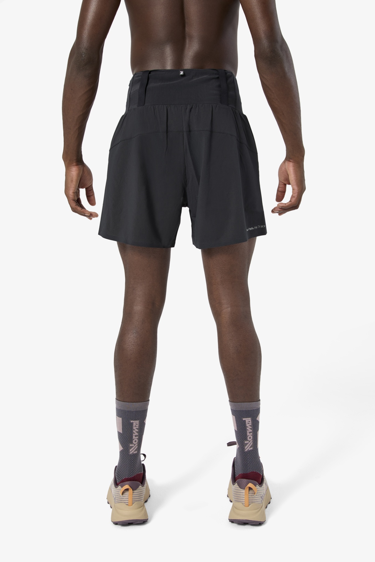 Homem com calções pretos, meias cinzentas e sapatilhas bege visto de costas