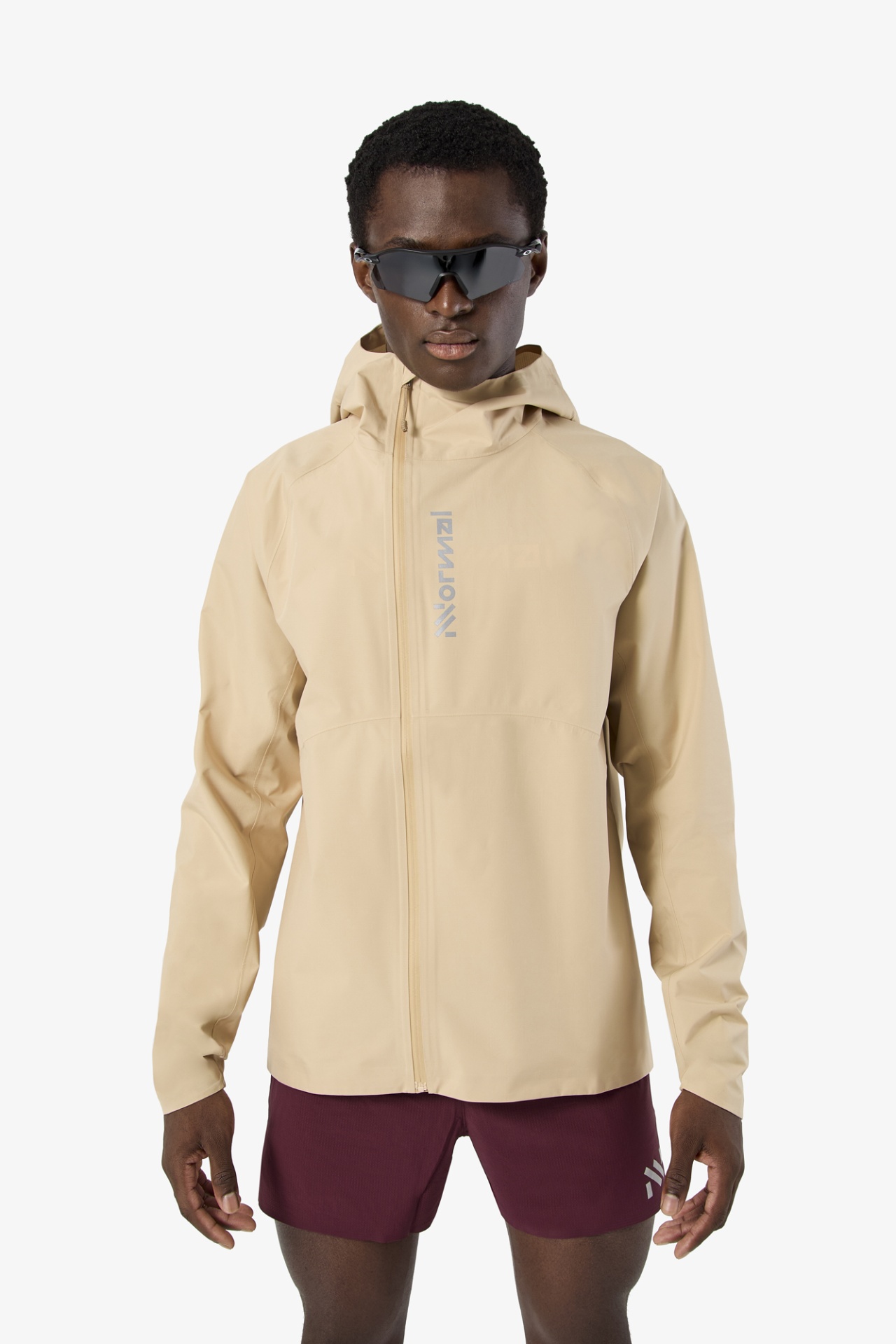 Homem com casaco bege com capuz e calções bordô com logótipo