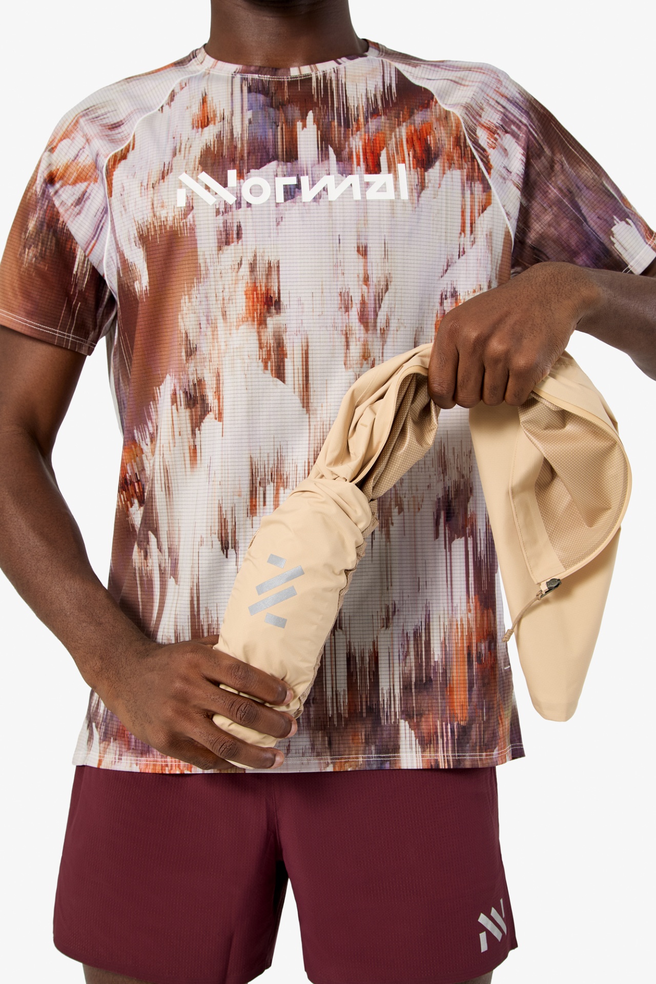 Pessoa com t-shirt estampada, calções vinho e segurando vestuário bege enrolado