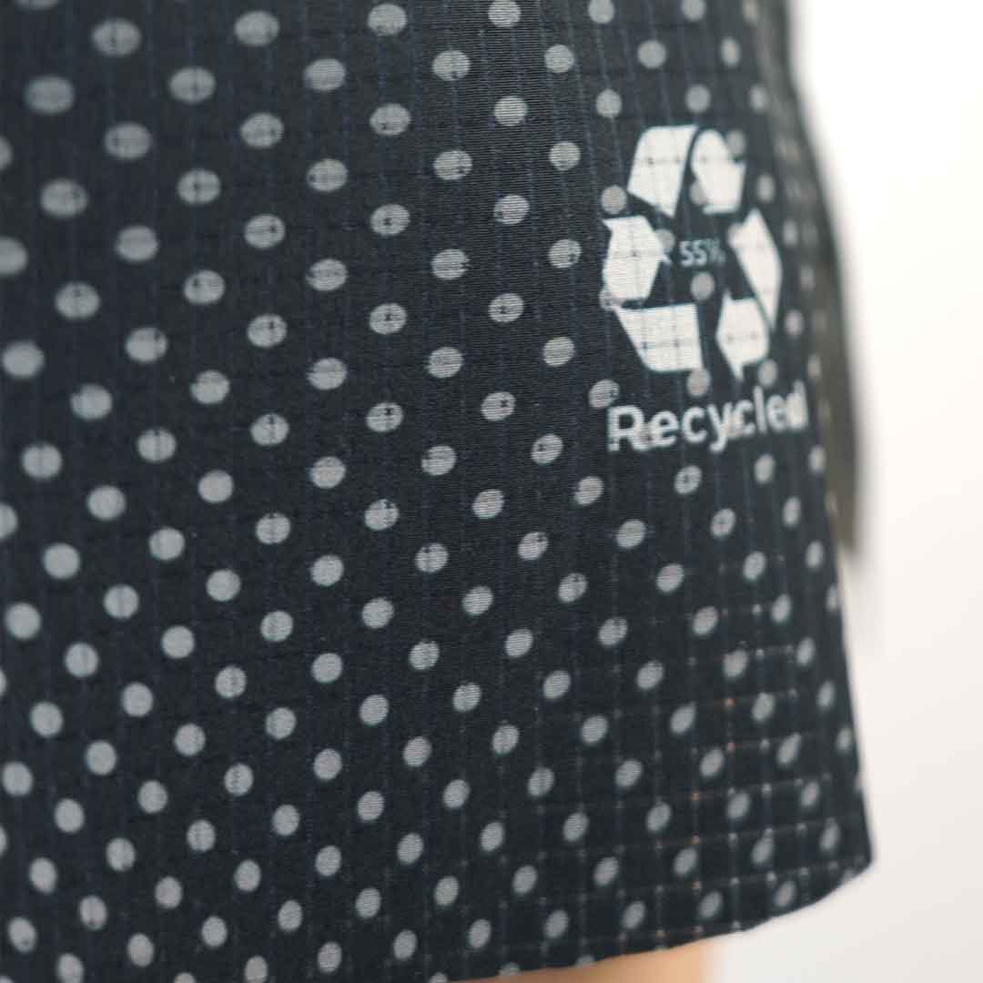 Tecido escuro com padrão de bolinhas brancas e símbolo de reciclagem com texto