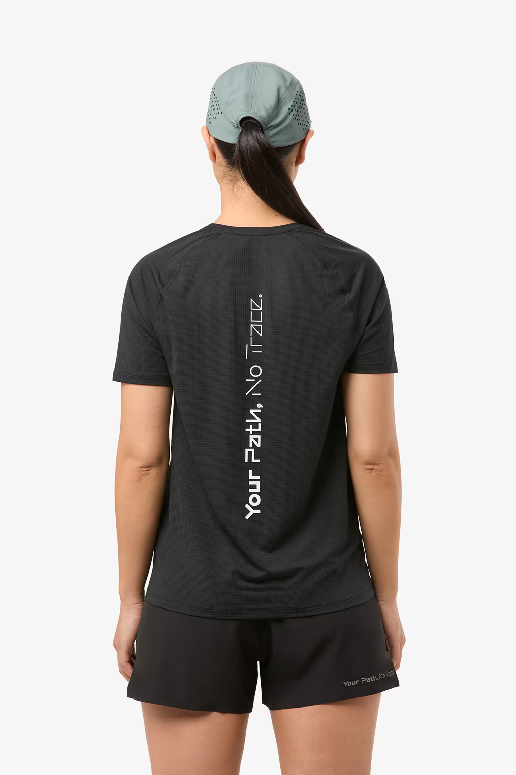 Pessoa de costas com boné verde azulado, t-shirt preta com texto vertical branco e calções pretos com texto