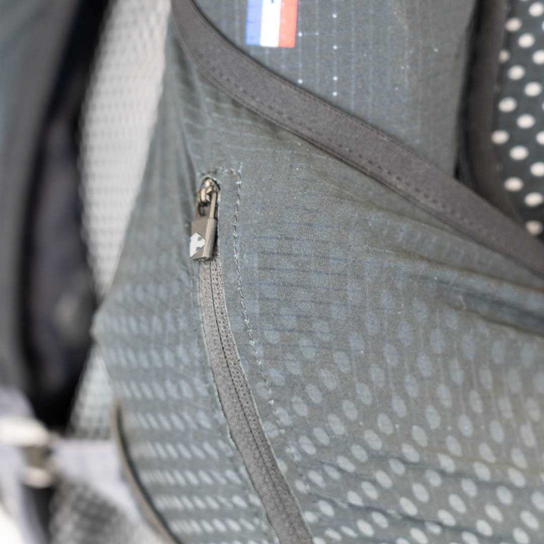 Mochila cinza com fecho de correr e detalhe da bandeira da França
