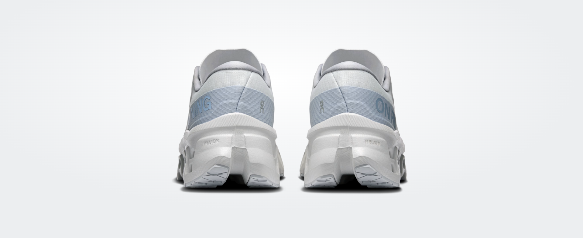 Ténis brancos e cinza-azulado vista traseira com texto ON RUNNING e HELION