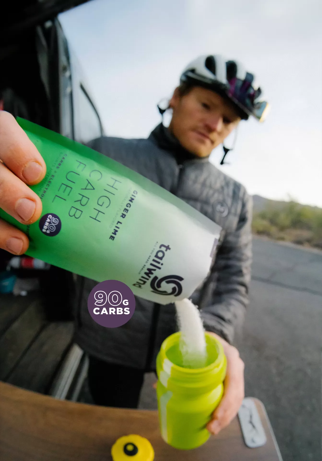 Pacote verde de suplemento a ser vertido em recipiente amarelo por ciclista com capacete e casaco cinzento ao ar livre