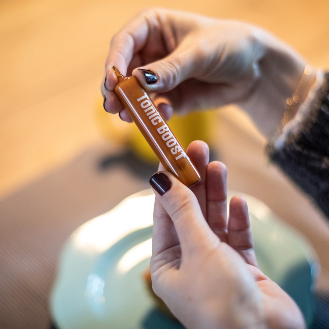 Mãos segurando um frasco marrom com texto 'TONIC BOOST'