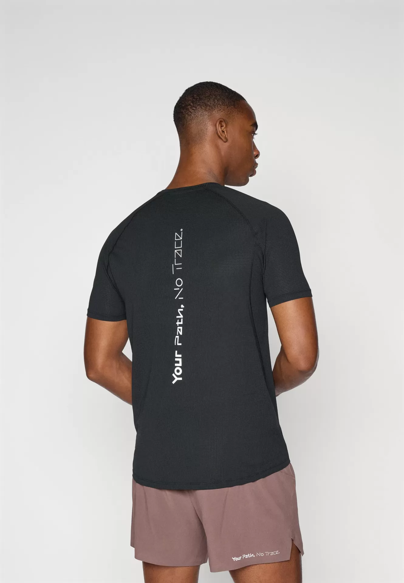 Homem de costas a usar t-shirt preta com texto branco e calções castanho azulado com texto branco