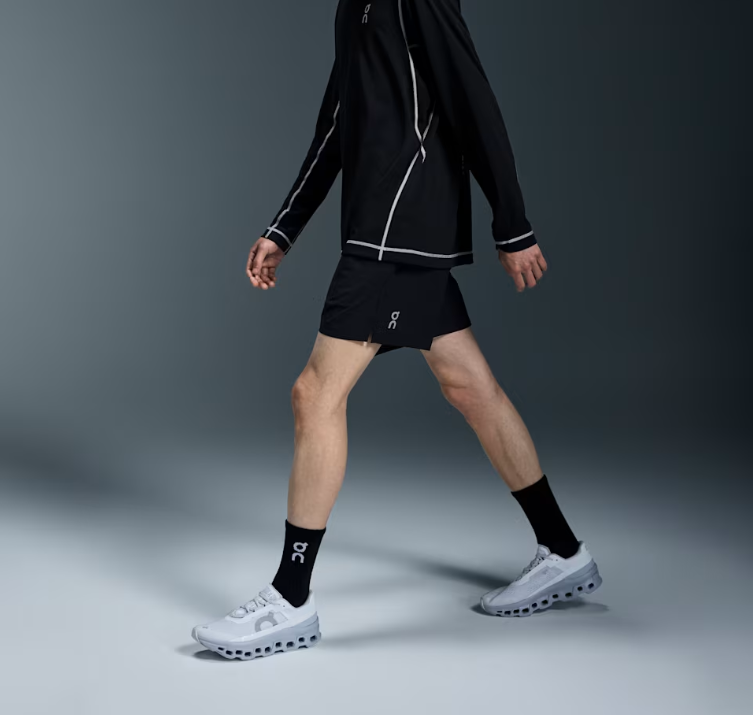 Homem a caminhar com roupa e ténis desportivos pretos e brancos com logótipo ON