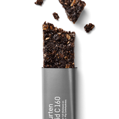 Barra de cereais castanha escura parcialmente embalada em embalagem cinzenta com texto branco