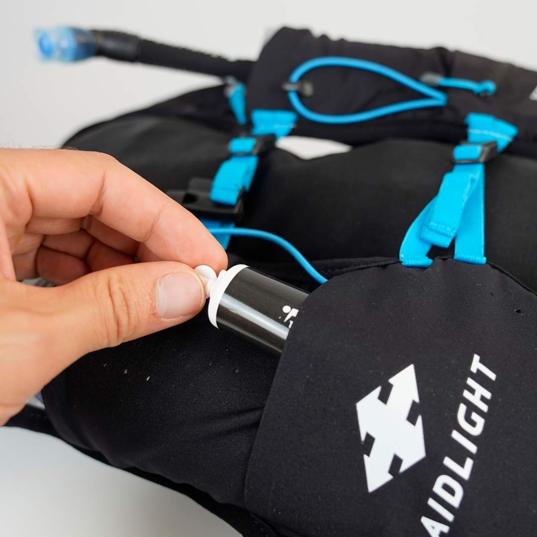 Mochila preta com acessórios azuis e logo RAIDLIGHT, mão a manusear tubo prateado