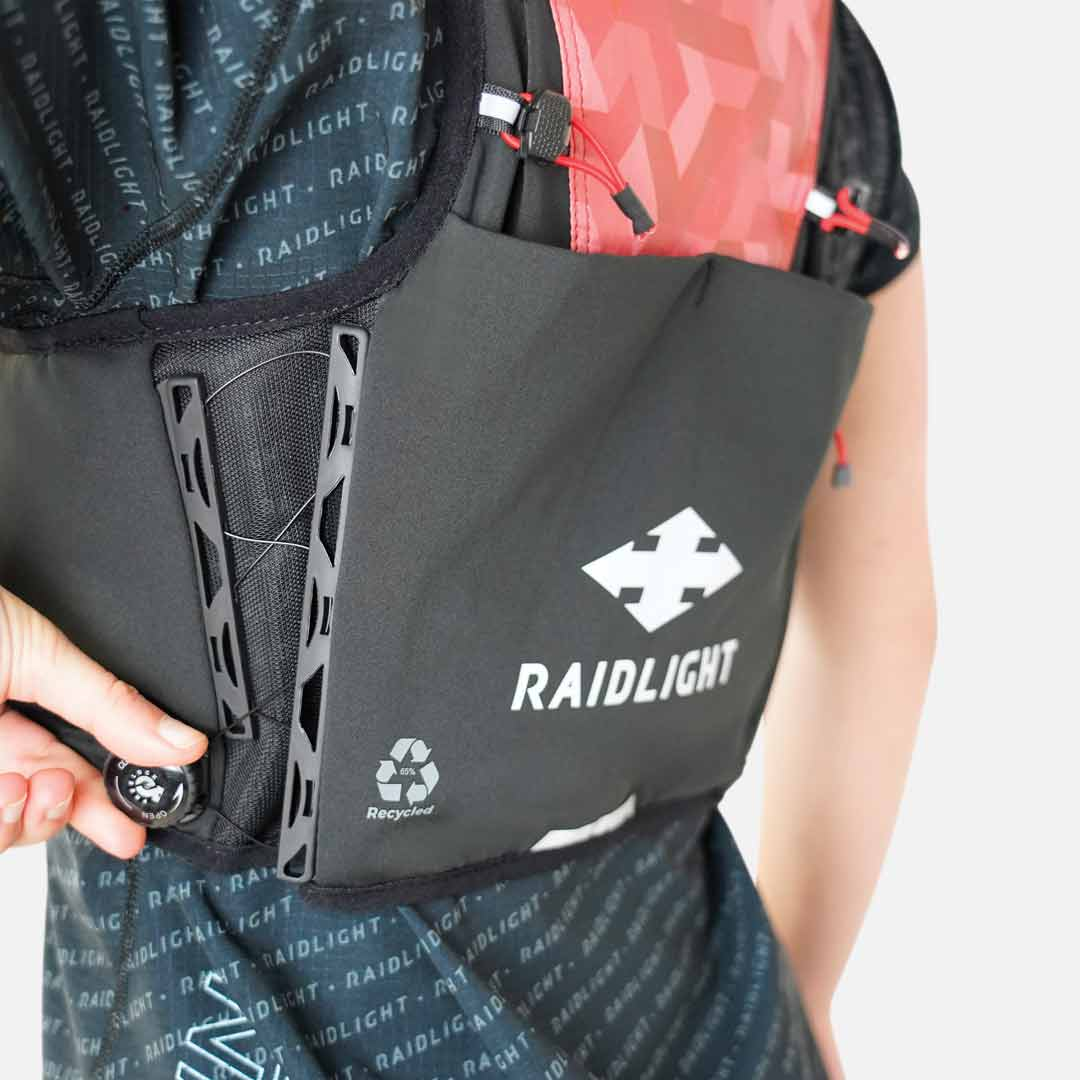 Mochila preta com logótipo RAIDLIGHT e bolso frontal, usada por pessoa com t-shirt preta com padrão RAIDLIGHT