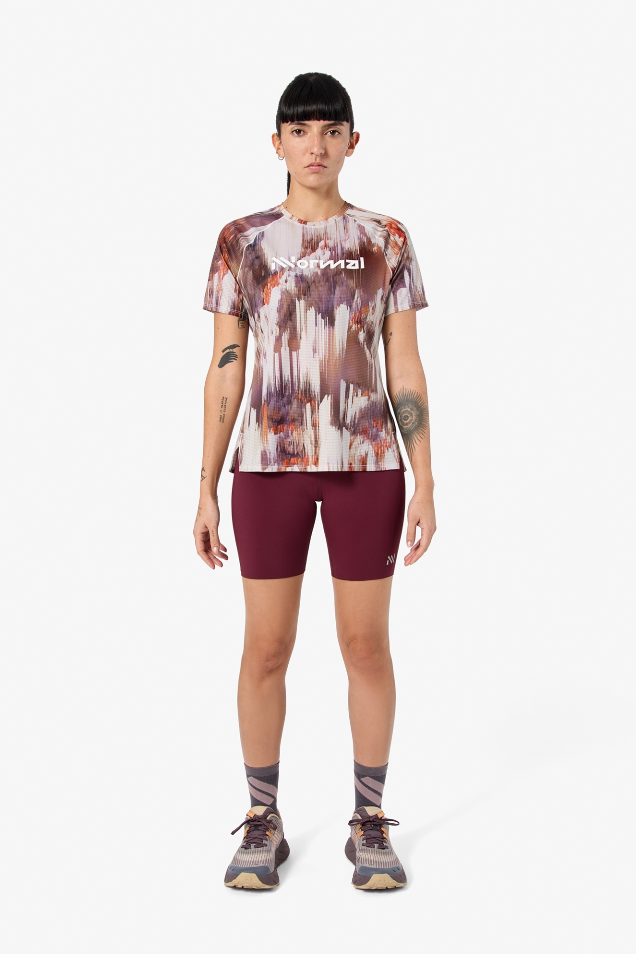 Mulher vestindo roupa desportiva com camiseta de padrão abstrato e calções bordeaux.
