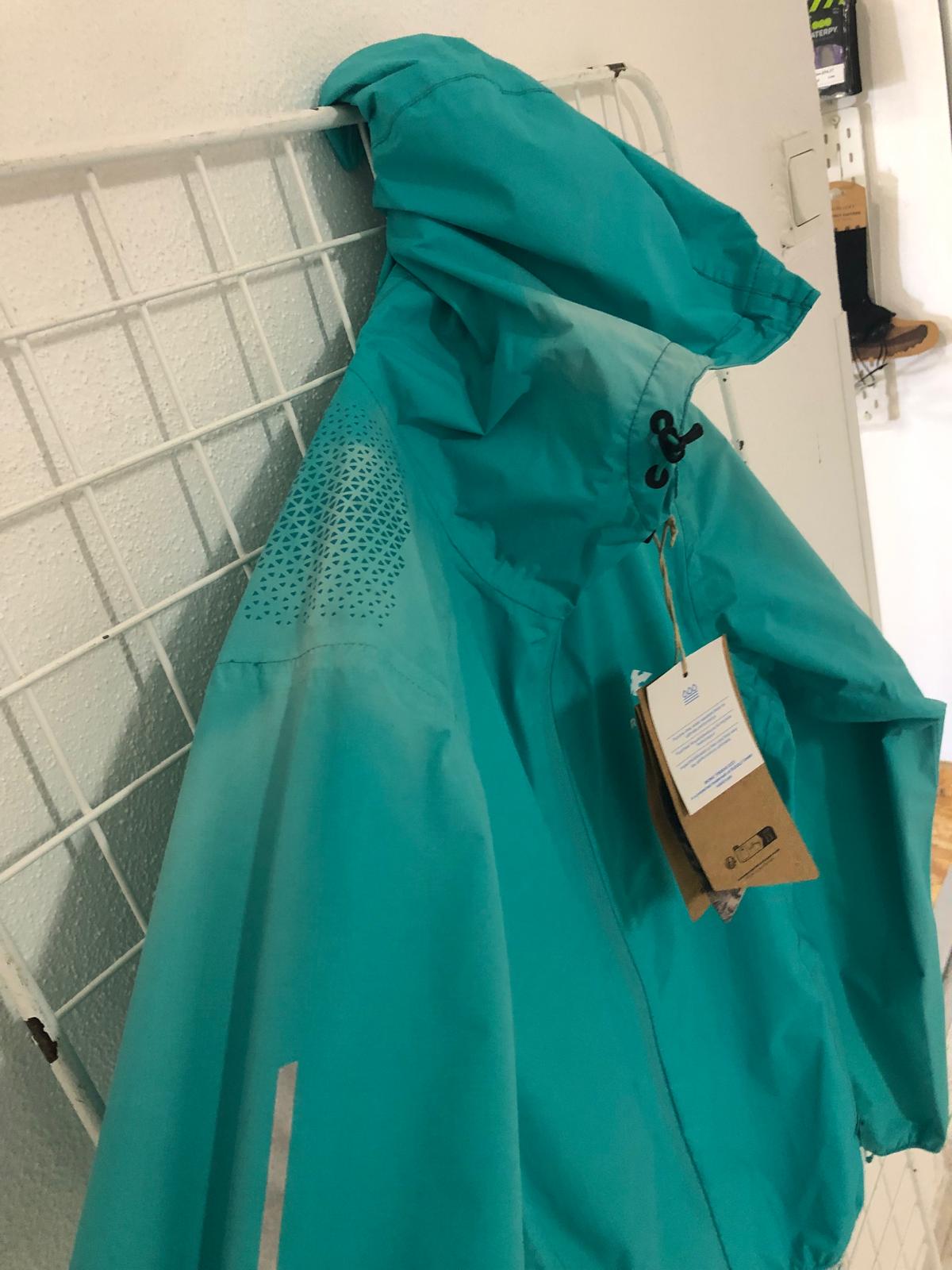 Casaco impermeável azul turquesa com capuz pendurado numa estrutura metálica branca