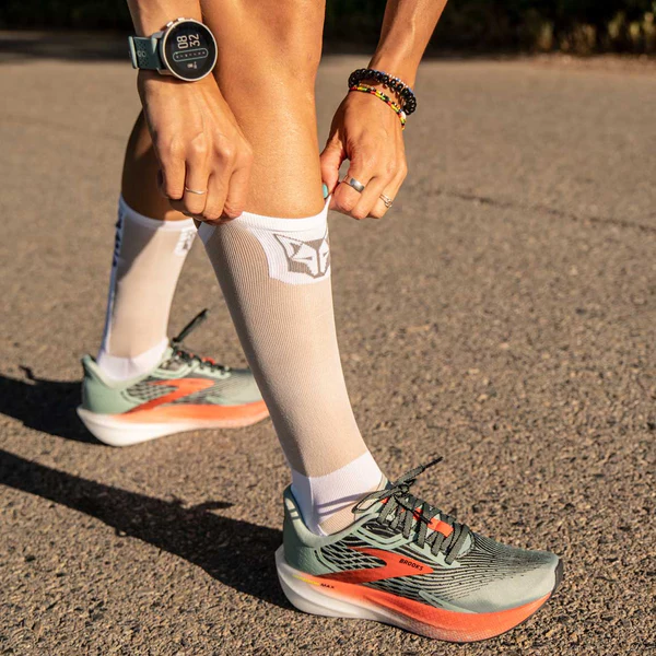 Ténis desportivos verdes e laranja com meias brancas e relógio no pulso