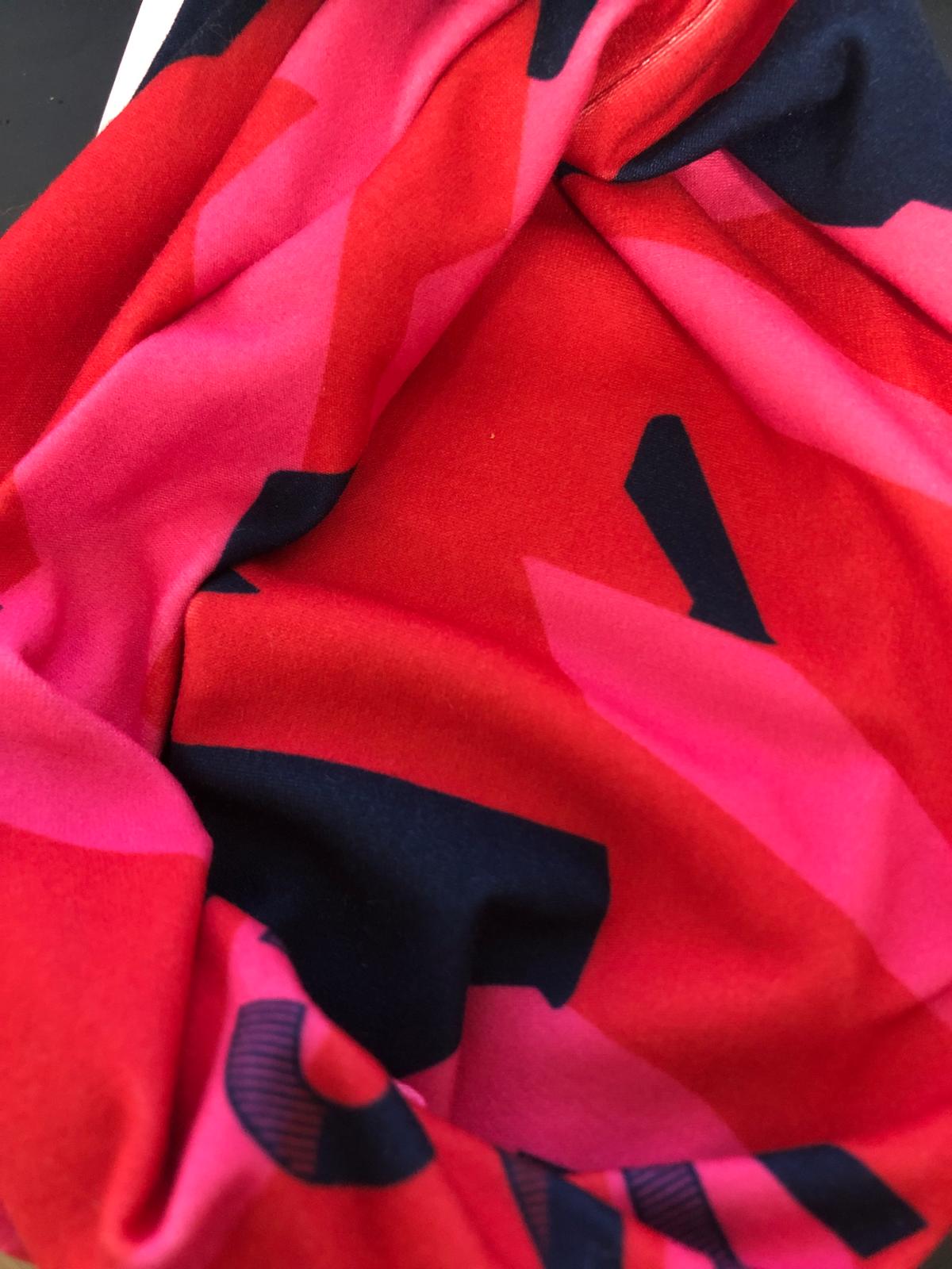 Tecido macio vermelho, rosa e preto com padrão geométrico e letras parciais