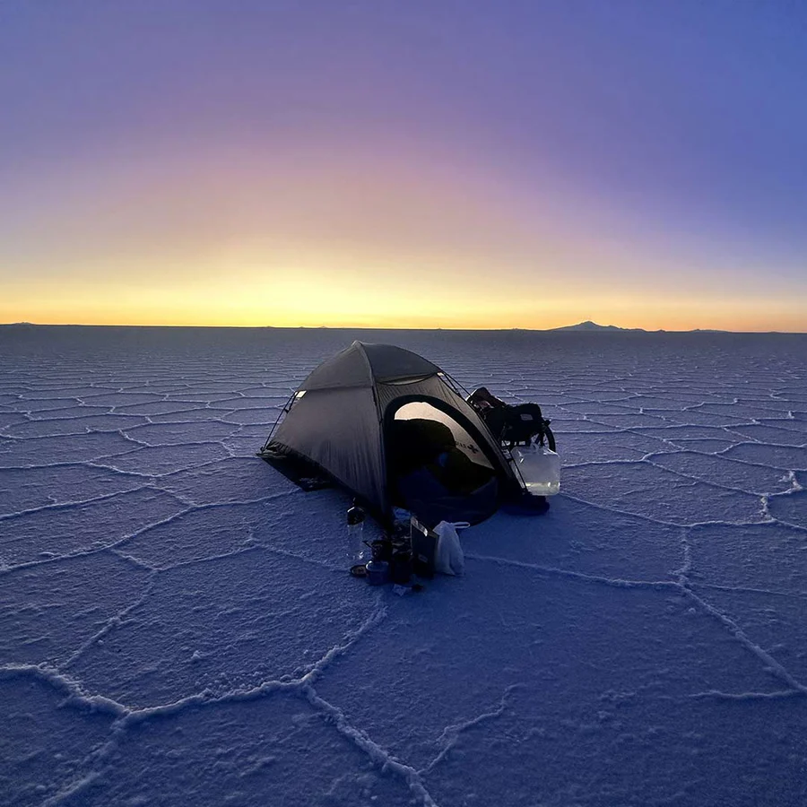 Tenda de campismo preta num terreno hexagonal azul e branco ao pôr do sol