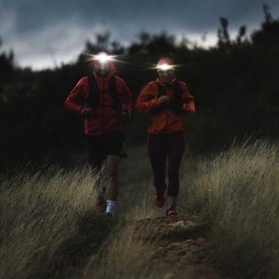 Duas pessoas a correr à noite num trilho com lanternas frontais acesas.
