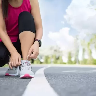 Pessoa a amarrar atacadores de sapatilhas desportivas cinza e rosa numa estrada ao ar livre