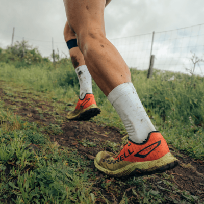 Sapatos de corrida Merrell laranja em trilho de terra com meias brancas