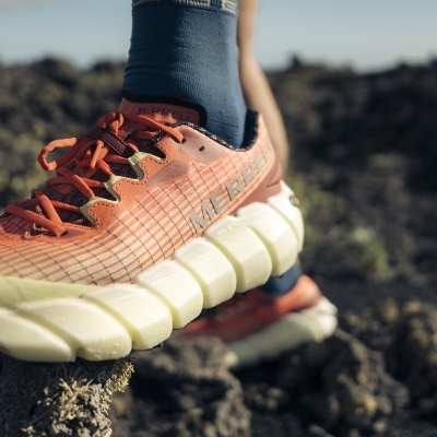 Ténis desportivo laranja com sola branca ondulada em ambiente rochoso