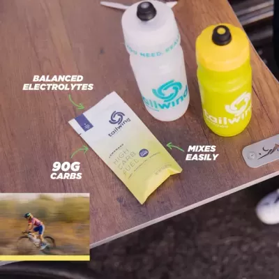 Dois bidões de desporto e um pacote de suplemento energético Tailwind sobre mesa de madeira