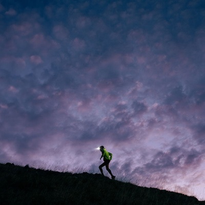 Pessoa a correr numa colina com roupa desportiva verde e luz de cabeça acesa ao anoitecer