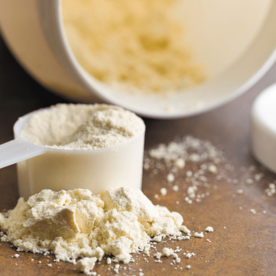 Colher com pó alimentar creme e pó espalhado junto a recipiente branco aberto