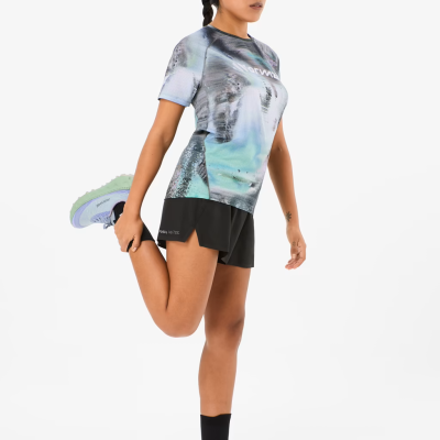 Mulher em roupa desportiva com t-shirt azul e cinza, calções pretos, boné preto e sapatilhas lilás.