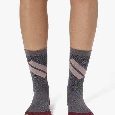 Par de meias cinza com detalhes bordô e faixa rosa em formato de S, usadas em pernas humanas.