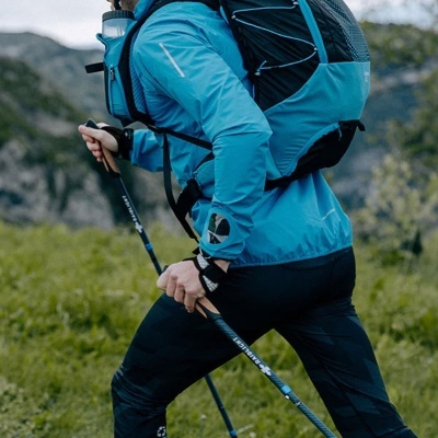 Pessoa com equipamento de caminhada azul e preta a usar bastões numa paisagem natural