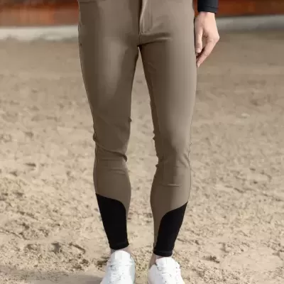 Calças de equitação bege com detalhes pretos e cinto preto, usadas com sapatos brancos, em chão de areia