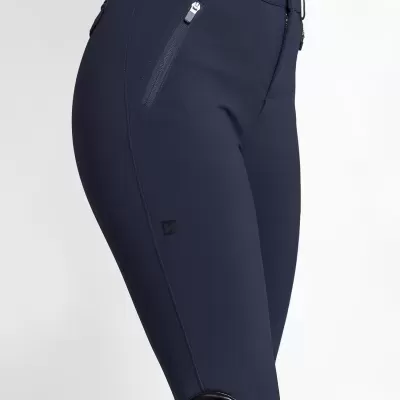 Calças justas azul escuro com fechos e logótipo, usadas com botas pretas com detalhes vermelhos.